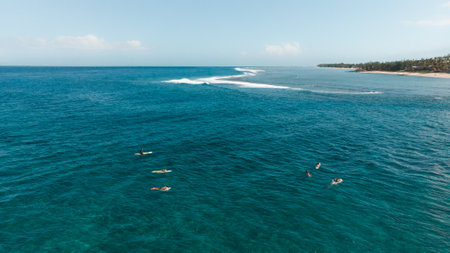 A breathtaking view of young surfers surfing in a turquoise sea on a sunny summer day