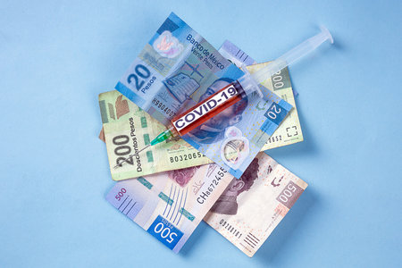 A syringe for covid-19 vaccination on top of Mexican peso banknotes on a blue backgroundの写真素材