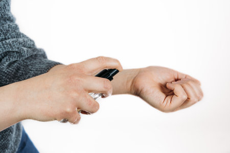 A closeup of  hands of a person testing the smell of perfume on white background