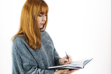 A redhead woman writing in a notebook with the left hand