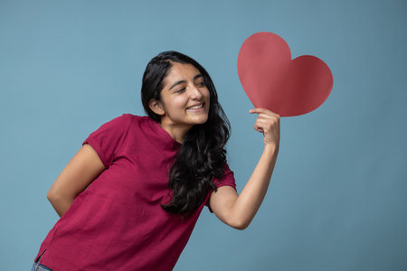 A Mexican Latin female holding  a red heart-shaped paper for valentine's dayの写真素材