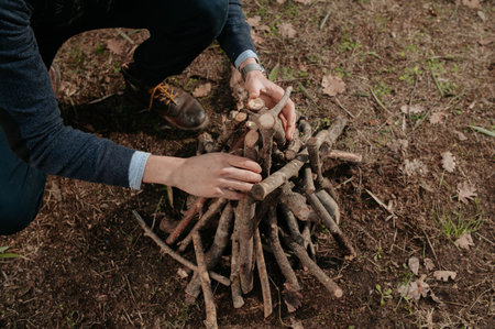 A close-up shot of a man's hands preparing a pile of firewood to light the fire in the forest