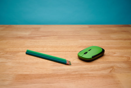 A closeup of a computer mouse and green pencils on a wooden deskの写真素材