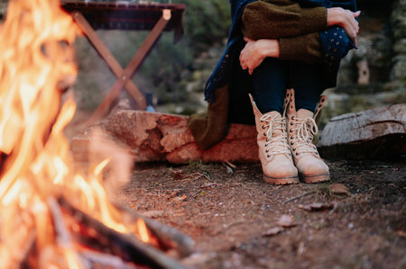 A person sitting on wood and holding her knees near a bonfire in a forestの写真素材