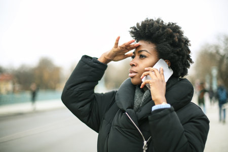 A young black female looking for someone while talking on her phone outsideの写真素材