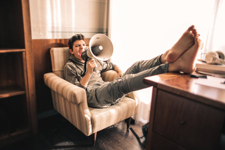 A barefoot boy with a grey outfit speaking on the speaker in his room