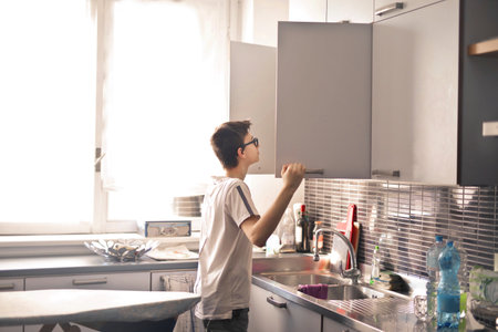 A boy with a white t-shirt and eyeglasses checking the shelves of their kitchenの写真素材
