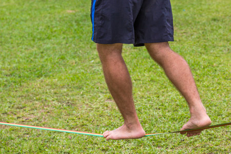 A male walking on a slackline in a green grassy fieldの写真素材