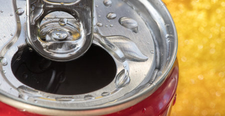 A closeup of open soda can with water drops on yellow bokeh background