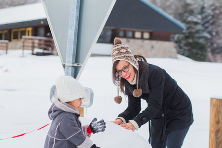 A Caucasian female with her daughter making a snowman and having fun