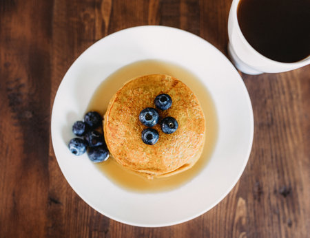 A top view of appetizing pancakes with blueberries on a white plate with a cup of coffeeの写真素材