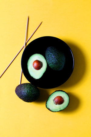 A fresh ripe Hass avocado in a dark bowl isolated on yellow background