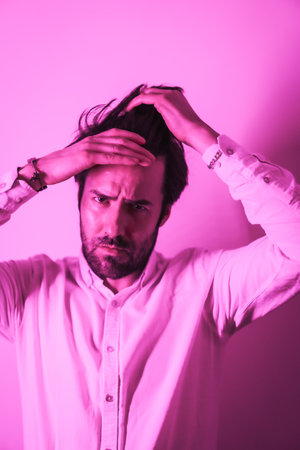 A vertical portrait of a handsome caucasian bearded young male touching his hairの写真素材