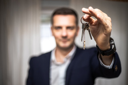 A Caucasian real estate agent holding keys to the house in selective focus