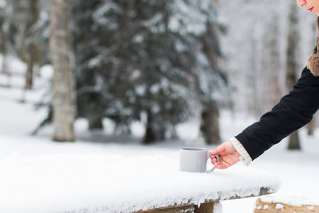 A female's hand taking the cup of tea from a wooden surface covered with snowの写真素材
