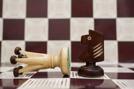 A close-up shot of a black wooden Knight next to a white fallen Queen on the chess boardの写真素材
