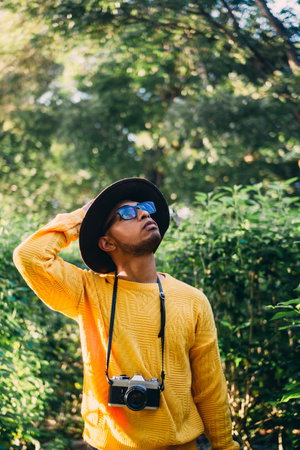 A vertical shot of a young Latin American man in a forest with a cameraの写真素材