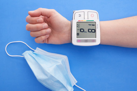 A person measuring his blood pressure with a blood pressure monitor on a blue background