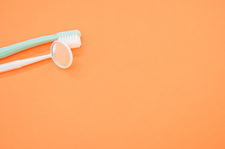 A closeup shot of a dental mirror with a toothbrush isolated on an orange backgroundの写真素材