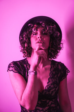 A caucasian curly female in an elegant dress and a hat posing on a purple club background