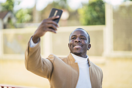 A shallow focus shot of a handsome African male taking a selfie with his smartphone