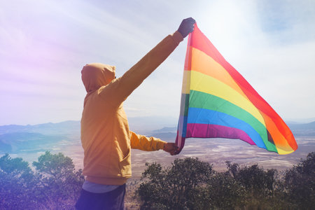 A man standing on top of the hill and holding the LGBT pride flagの写真素材