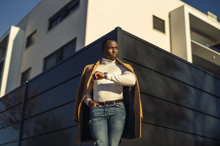 A low angle shot of a stylish handsome African male in a coat waiting for his friendの写真素材