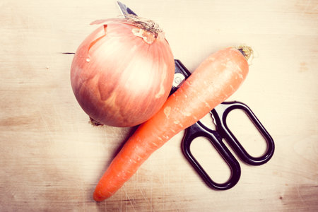 A closeup shot of fresh onion, carrot, and scissors on a wooden surfaceの写真素材