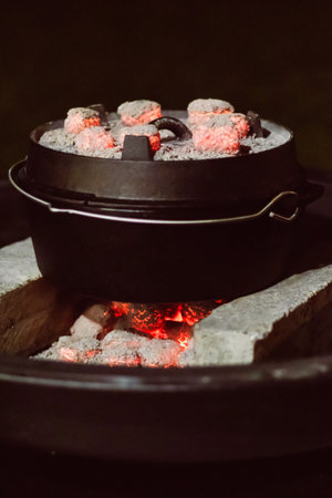 A black dutch oven with red glowing coal on it and underneath.の写真素材