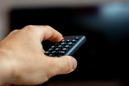 A male hand holding a TV remote and trying to turn on the TV
