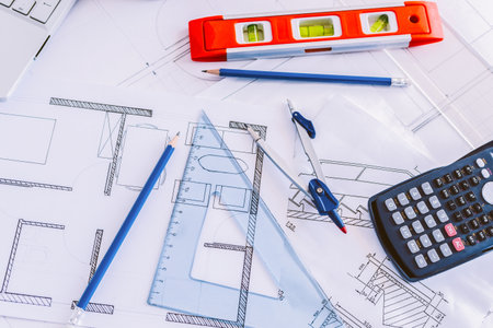 A top view of drawing sketch plans, blueprints, ruler, calculator, and pencils on a working desk
