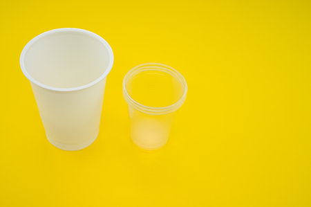 A high angle shot of big and small plastic cups on a yellow surfaceの写真素材
