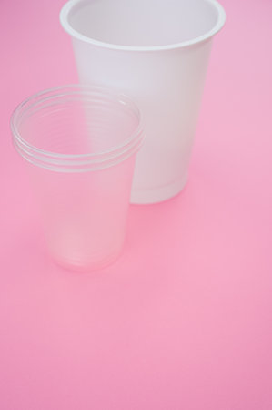 A vertical shot of big and small plastic cups on a pink surfaceの写真素材