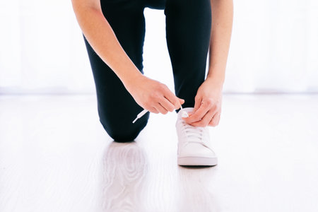 A shallow focus of a sporty man tying his white sneaker on light background