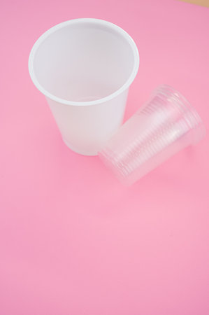 A vertical shot of big and small plastic cups on a pink surface