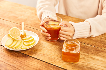 A female holding a cup of hot tea with honey, lemon and ginger - home treatmentの写真素材