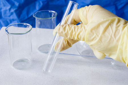 A hand in glove holding empty laboratory glassware on the sterile table