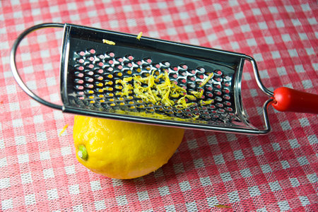 A closeup of a grating fresh lemon on a red checkered surface