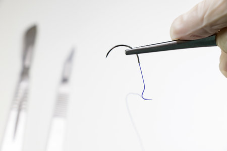 A selective focus of a hand in gloves holding with surgical tweezers absorbable suture
