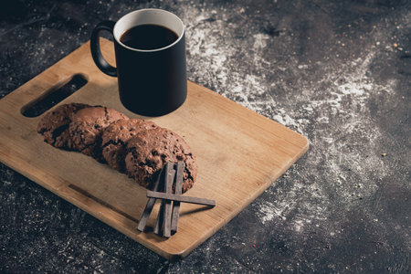 A closeup shot of fresh chocolate cookies and a cup of coffee on a wooden tableの写真素材