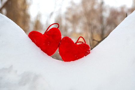 Valentine's Day, two red hearts lie on a slide of white snow on a gray abstract backgroundの写真素材