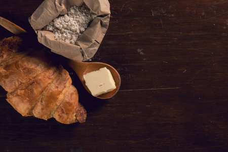 An overhead shot of croissants on a wooden table with butter and a flour bagの写真素材