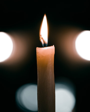 A vertical shot of a brightly burning candle against a dark blurry background