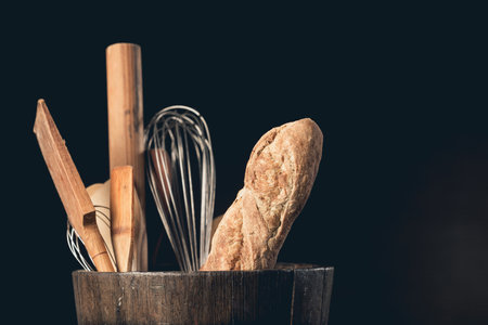 A closeup shot of bakery utensils with baguette in a wooden pot on a black backgroundの写真素材