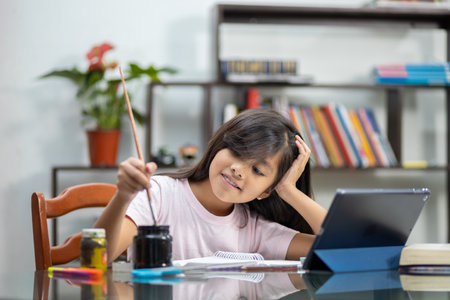 A pretty Hispanic schoolgirl painting on her notebook with a brush at home - online education