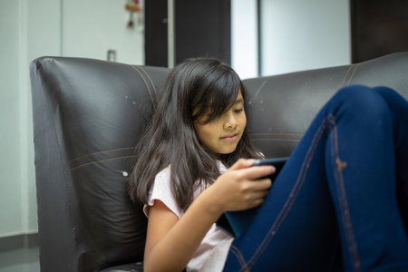 A pretty Hispanic girl studying online with tablet while lying on the armchair - online educationの写真素材