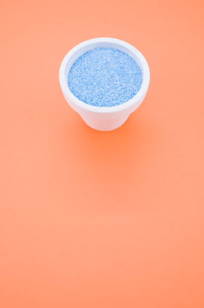 A vertical shot of blue sand in a small cup isolated on an orange backgroundの写真素材