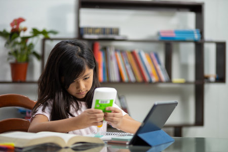 A little Hispanic schoolgirl glui paper for her homework at home - online educationの写真素材