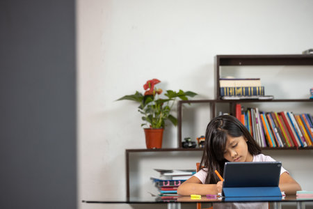 A pretty Hispanic schoolgirl writing concentrated on her notebook at home - online educationの写真素材