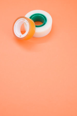 A vertical shot of two rolls of sticky tapes isolated on an orange background